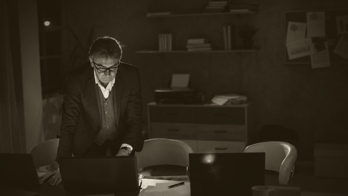 Dirigeant d’entreprise travaillant seul tard le soir dans un bureau sombre, illustrant la pression et les responsabilités quotidiennes des entrepreneurs.